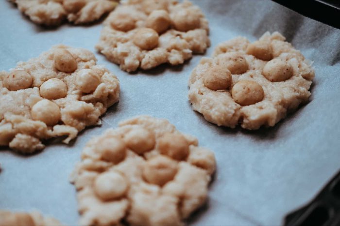 Makadamové sušenky na plechu. Neupečené zdravé sušenky na plechu dozdobte upraženými makadamovými ořechy.